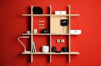 Photo of Stylish wooden shelves with photography equipment and decorative elements on red wall