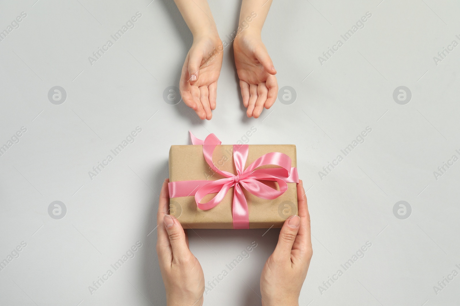 Photo of Mother giving gift box to her child on light gray background, top view