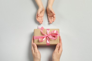 Mother giving gift box to her child on light gray background, top view