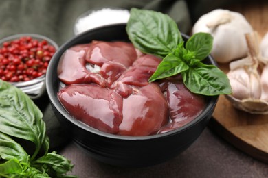 Photo of Bowl of raw chicken liver with basil on grey table, closeup