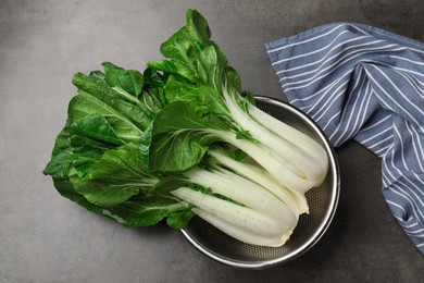 Photo of Fresh green pak choy cabbages with water drops in sieve on grey table, top view