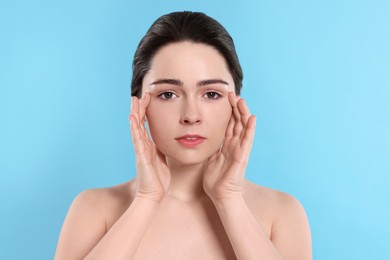 Photo of Young woman massaging her face on turquoise background