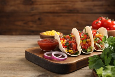 Photo of Tasty tacos with vegetables on wooden table, closeup. Space for text