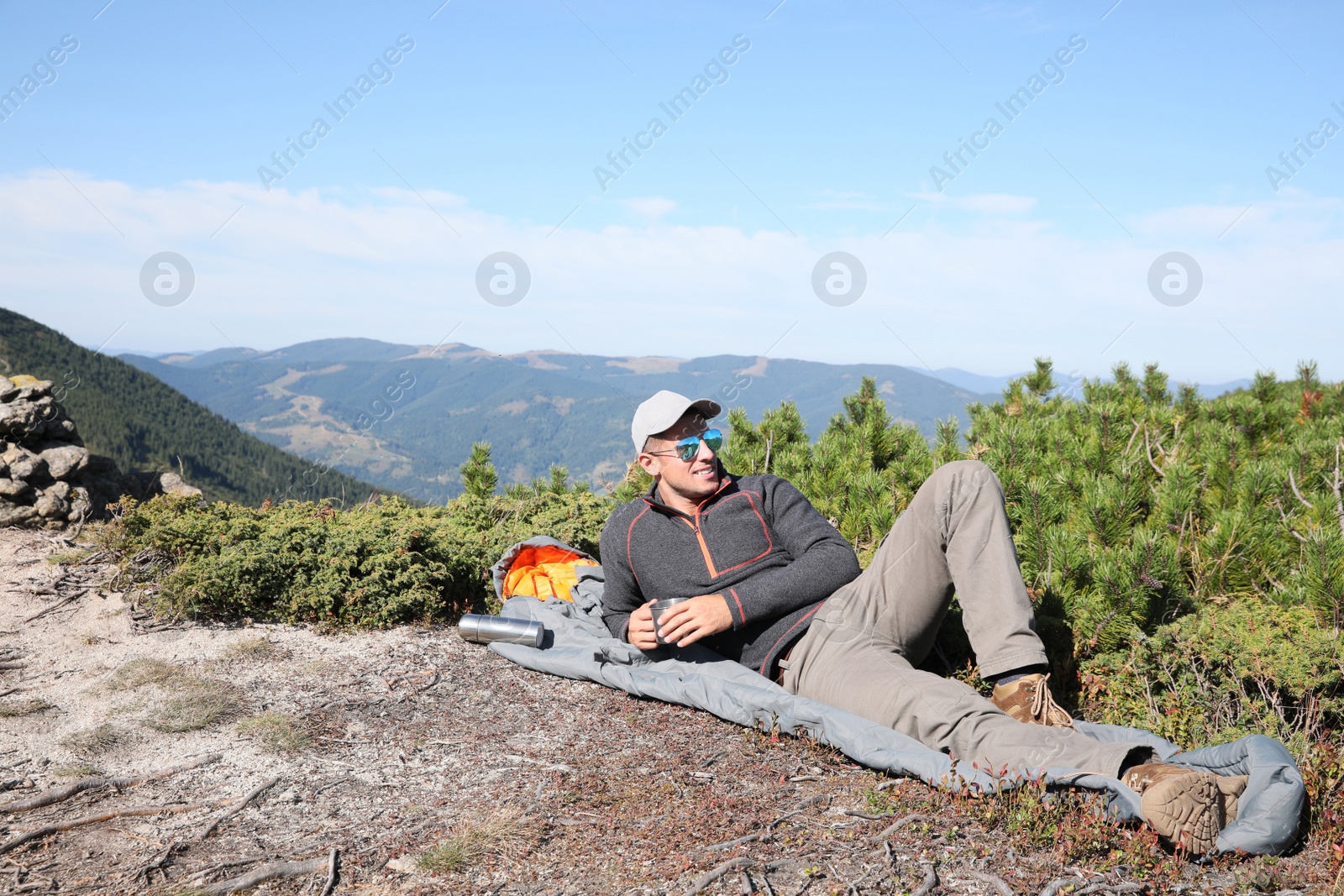 Photo of Tourist with hot drink and sleeping bag on mountain peak
