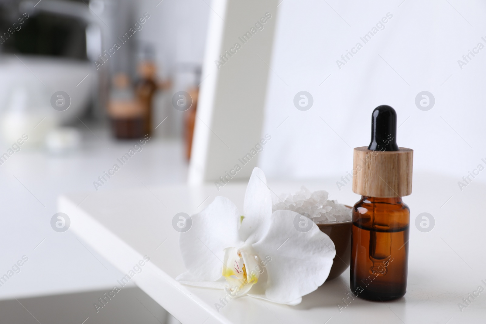 Photo of Bottle of essential oil, orchid flower and sea salt on white shelf in bathroom, closeup. Space for text