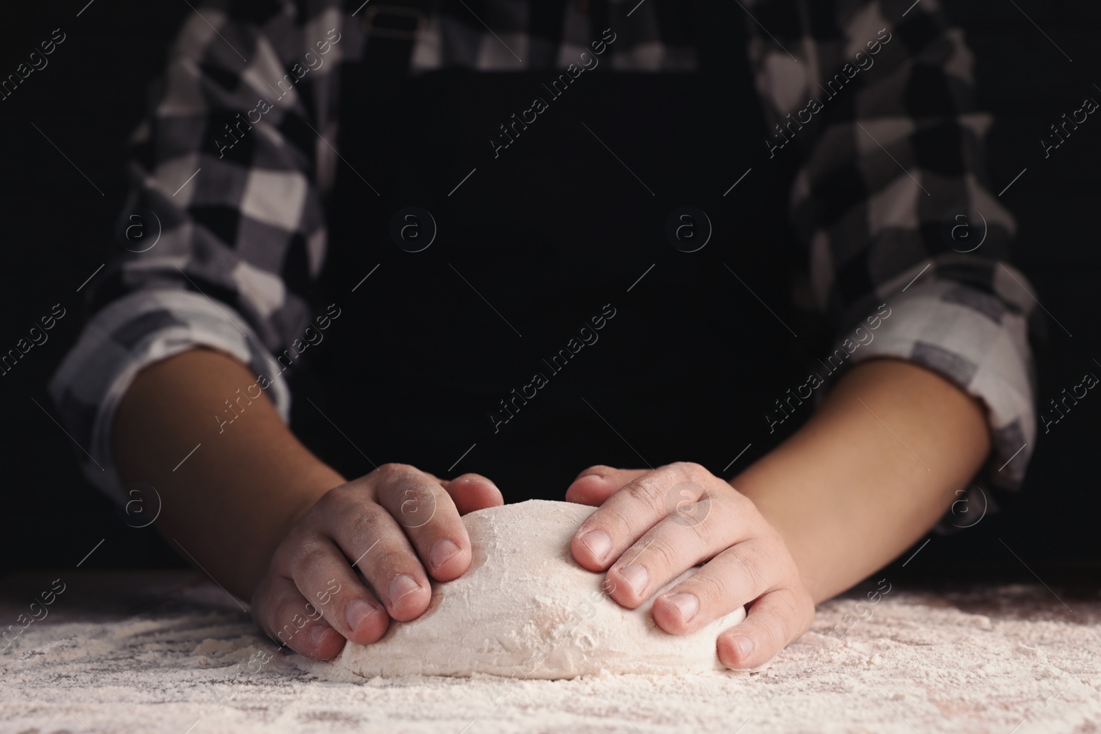 Photo of Man kneading dough at wooden table on dark background, closeup