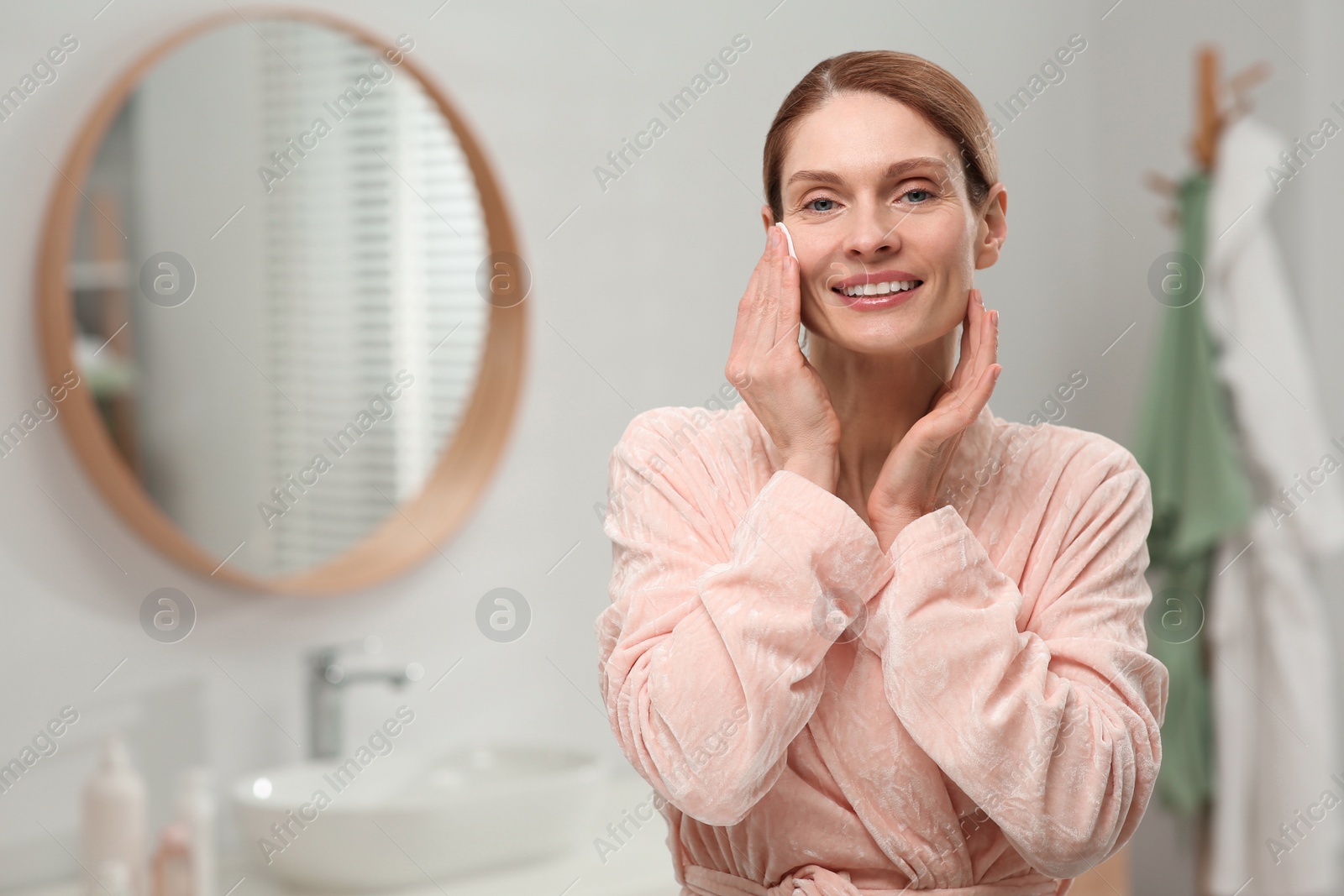 Photo of Beautiful woman removing makeup with cotton pad indoors, space for text