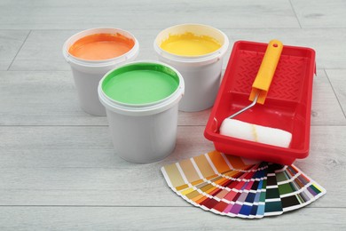 Photo of Buckets of paints, palette and decorator's tools on light wooden background