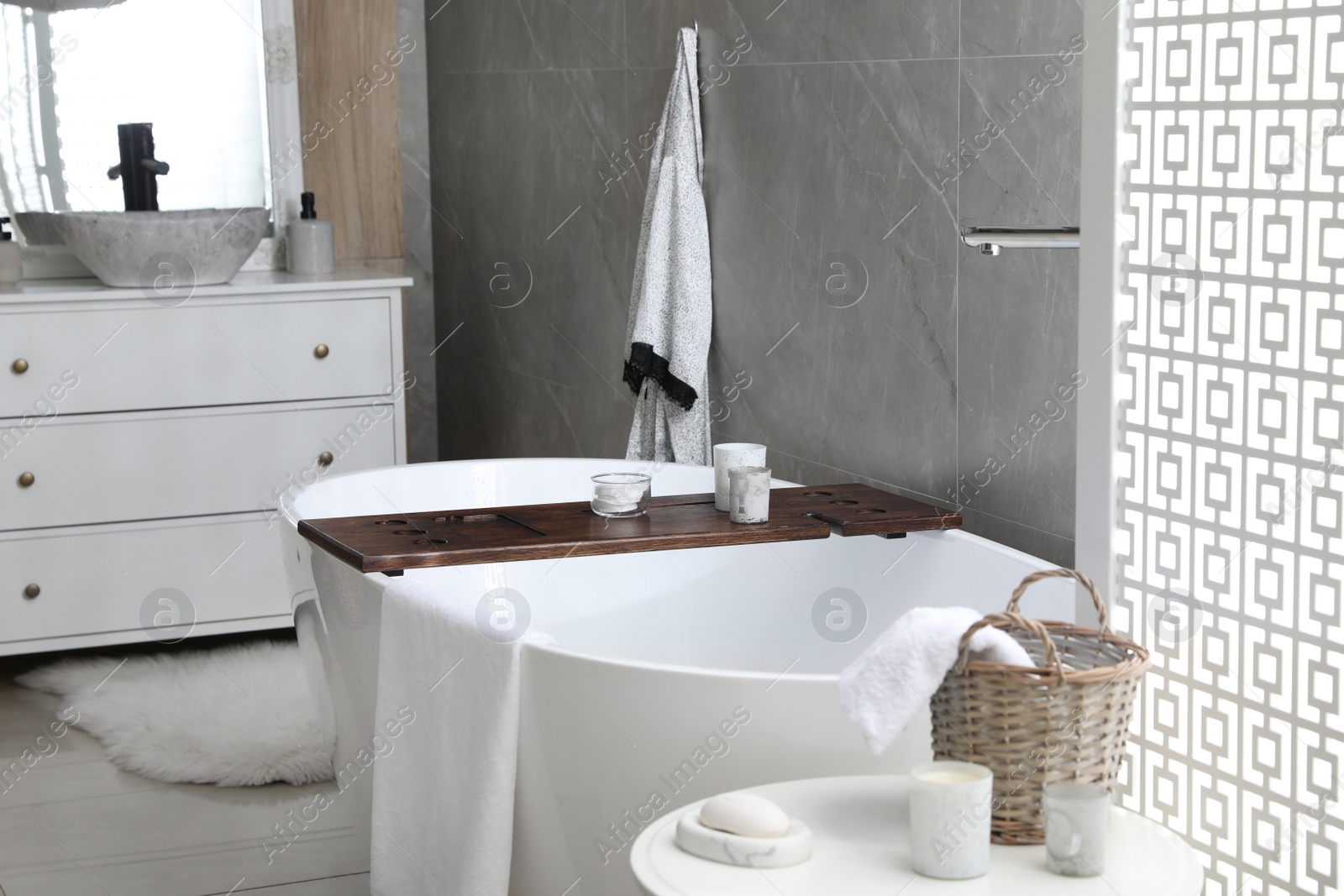 Photo of Modern white tub and table with toiletries in bathroom. Interior design