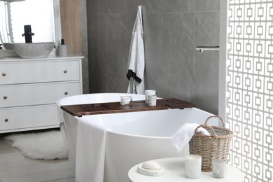 Modern white tub and table with toiletries in bathroom. Interior design