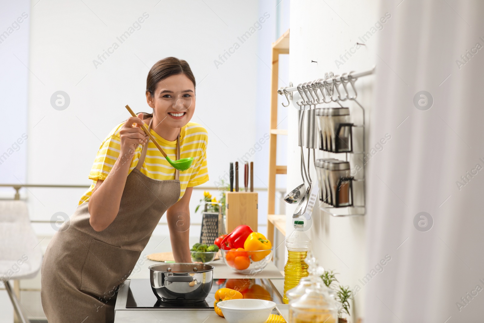 Photo of Young woman cooking tasty soup in kitchen