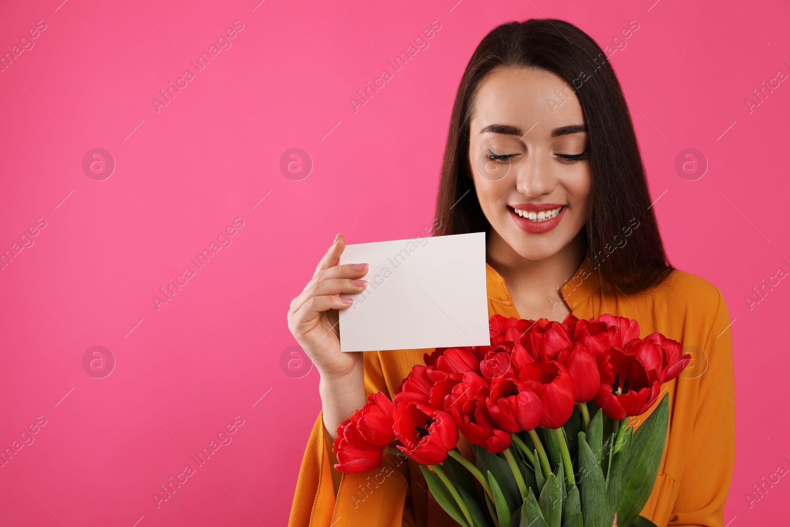 Photo of Happy woman with red tulip bouquet and greeting card on pink background, space for text. 8th of March celebration