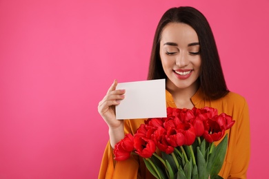 Photo of Happy woman with red tulip bouquet and greeting card on pink background, space for text. 8th of March celebration