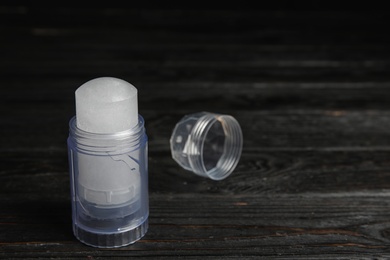 Photo of Natural crystal alum deodorant and cap on black wooden table, space for text