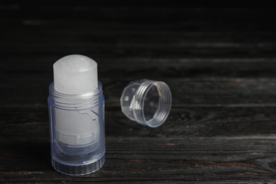 Natural crystal alum deodorant and cap on black wooden table, space for text