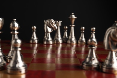Photo of Many chess pieces on wooden checkerboard against black background, selective focus