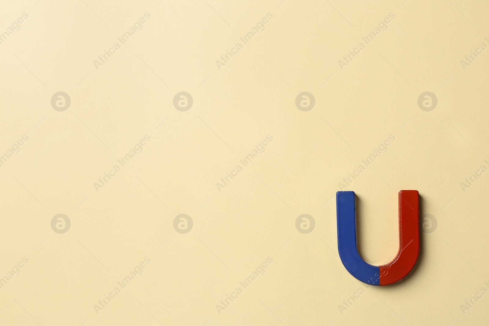 Photo of Red and blue horseshoe magnet on light beige background, top view. Space for text