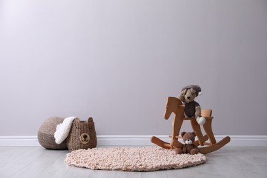 Photo of Rocking horse with toys and wicker basket near light grey wall in child room. Interior design