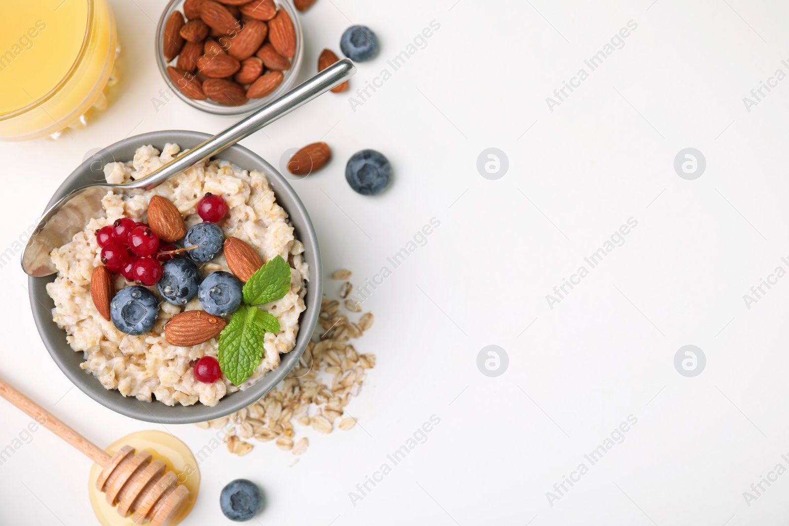 Photo of Oatmeal served with berries, almonds and honey on white background, flat lay. Space for text