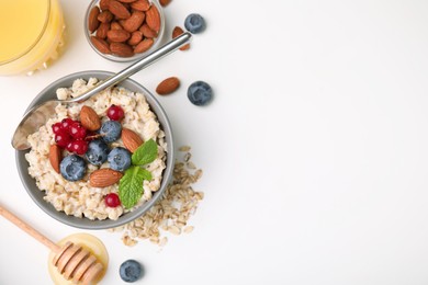 Oatmeal served with berries, almonds and honey on white background, flat lay. Space for text