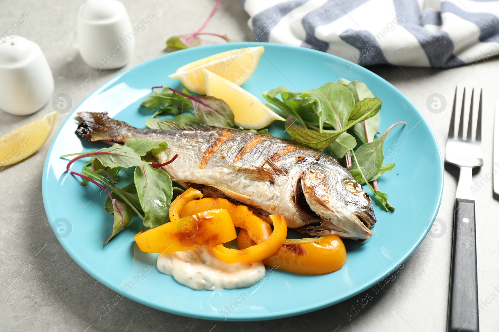 Photo of Delicious roasted fish with lemon and vegetables on grey table