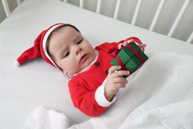 Photo of Cute baby wearing festive Christmas costume with gift box in crib