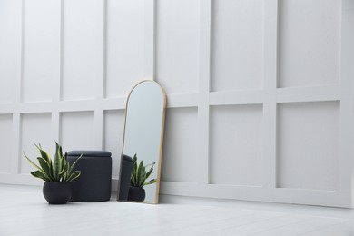 Photo of Stylish mirror, pouf and houseplant near white wall, space for text. Interior accessories