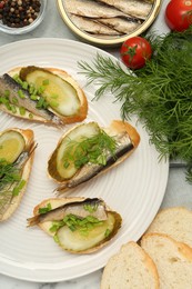 Photo of Delicious sandwiches with sprats, pickled cucumber, green onion and dill served on table, flat lay