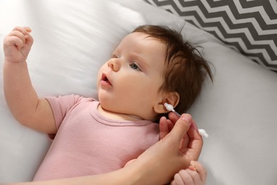 Photo of Mother cleaning ears of her baby with cotton bud on bed, closeup