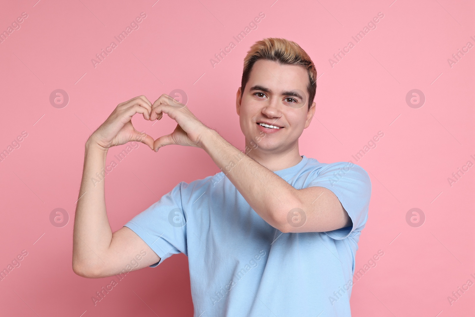 Photo of Young man showing heart gesture with hands on pink background
