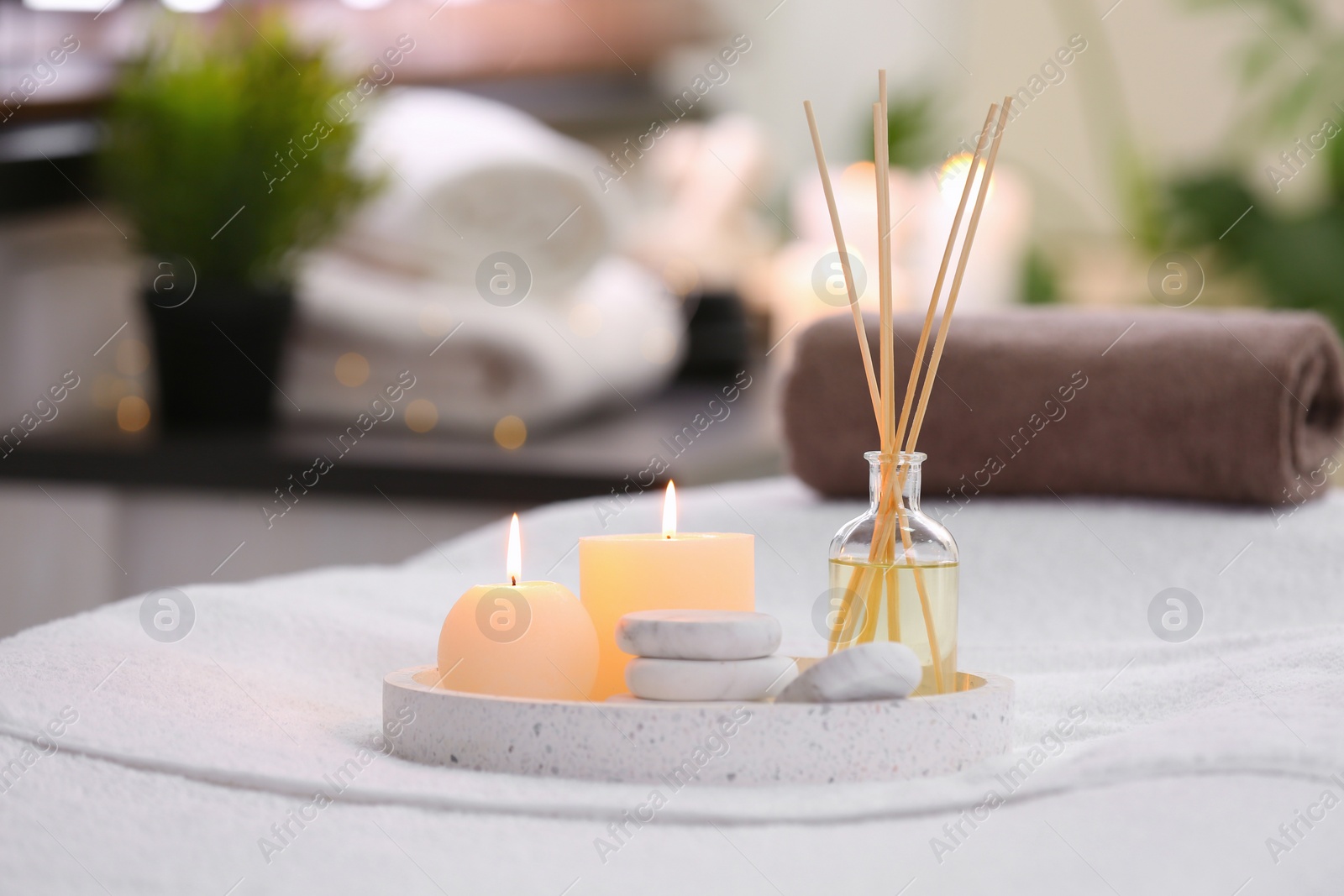 Photo of Composition with reed air freshener, candles and stones on massage table in spa salon