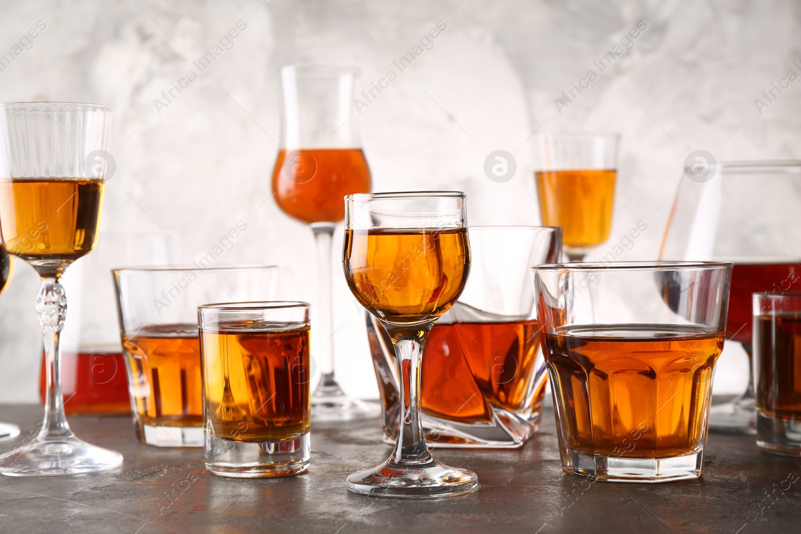 Photo of Different delicious liqueurs in glasses on grey table