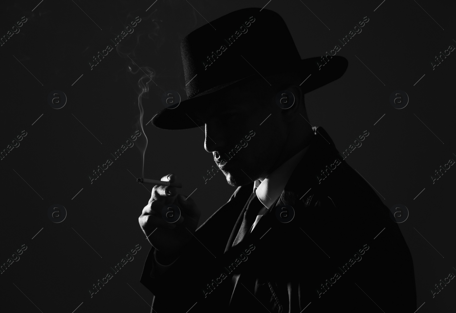 Photo of Old fashioned detective smoking cigarette on dark background, black and white effect