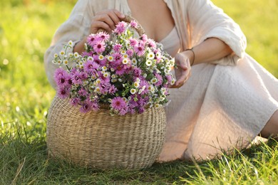 Photo of Woman holding wicker basket with beautiful wild flowers outdoors, closeup