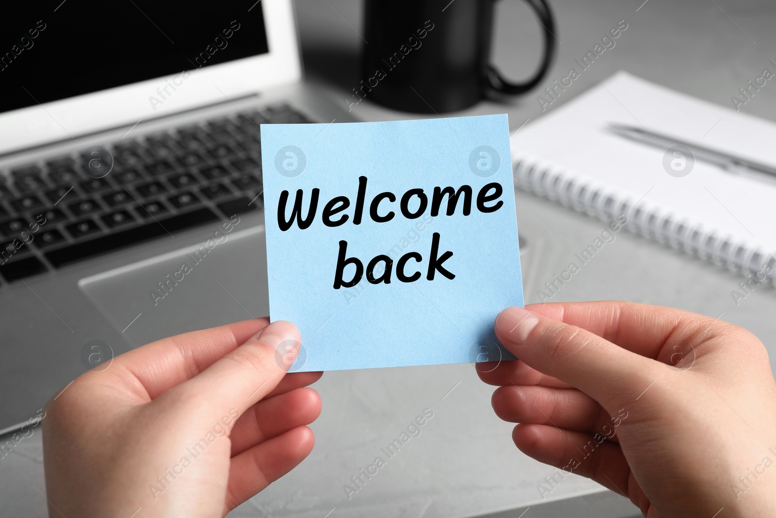 Image of Woman holding paper note with phrase Welcome Back at her office desk, closeup