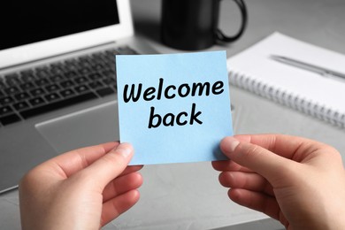 Image of Woman holding paper note with phrase Welcome Back at her office desk, closeup