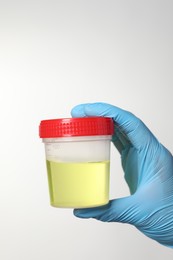 Photo of Doctor holding container with urine sample for analysis on white background, closeup