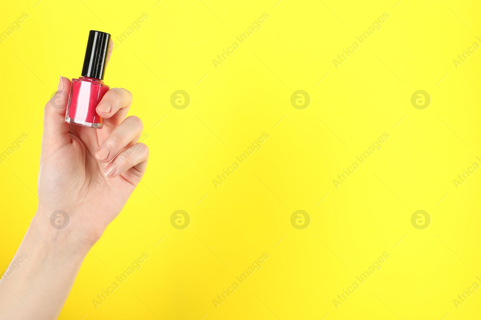 Photo of Woman holding nail polish on yellow background, closeup. Space for text