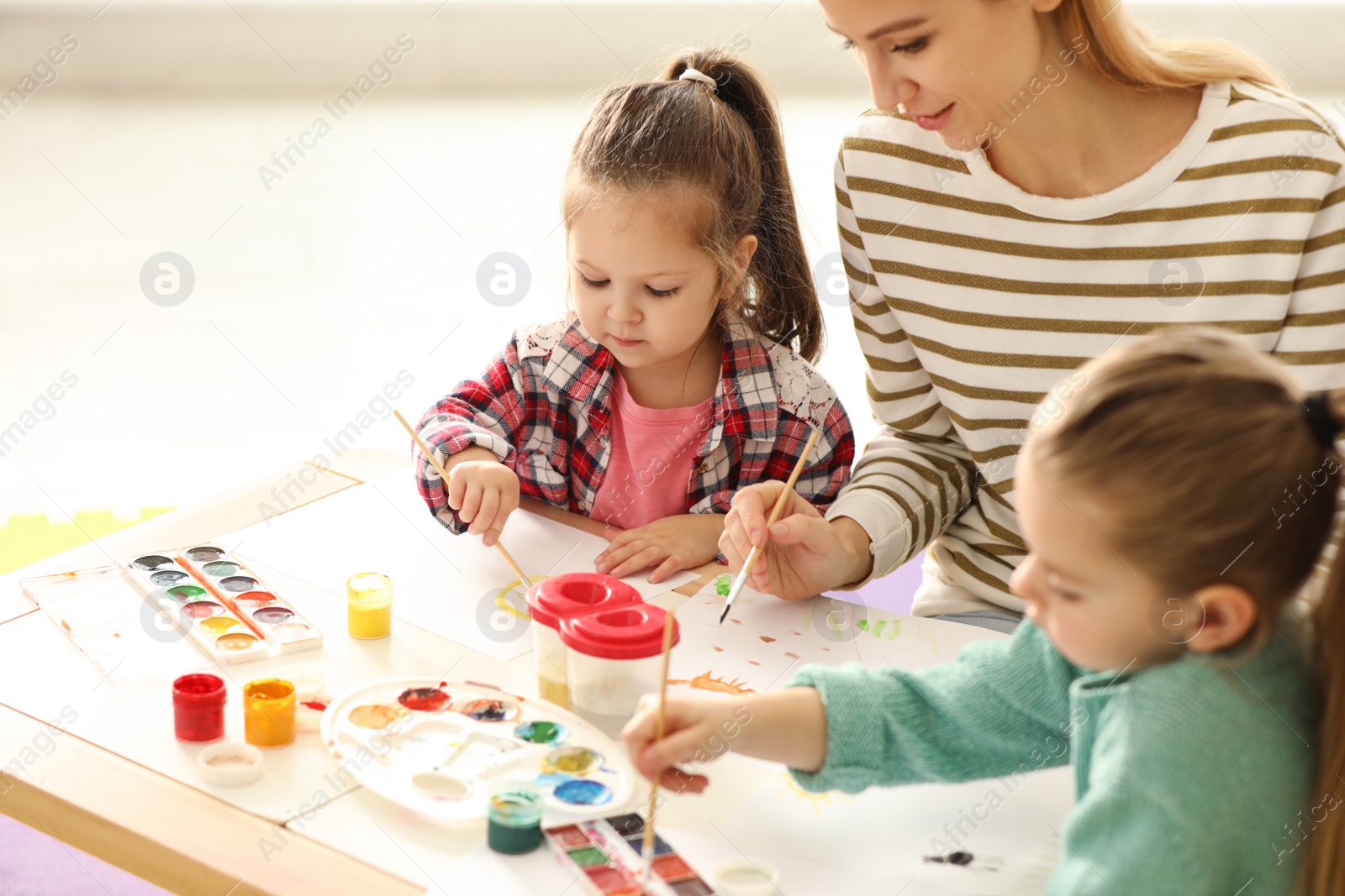 Photo of Mother and daughters painting at table indoors. Playing with children