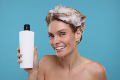 Washing hair. Portrait of beautiful happy woman with bottle on light blue background