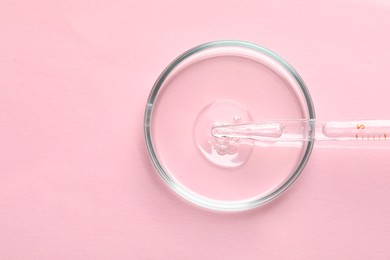 Glass pipette and petri dish with liquid on pink background, top view. Space for text