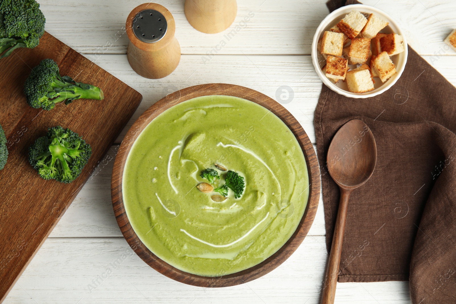 Photo of Delicious broccoli cream soup served on white wooden table, flat lay