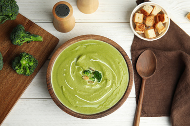 Photo of Delicious broccoli cream soup served on white wooden table, flat lay