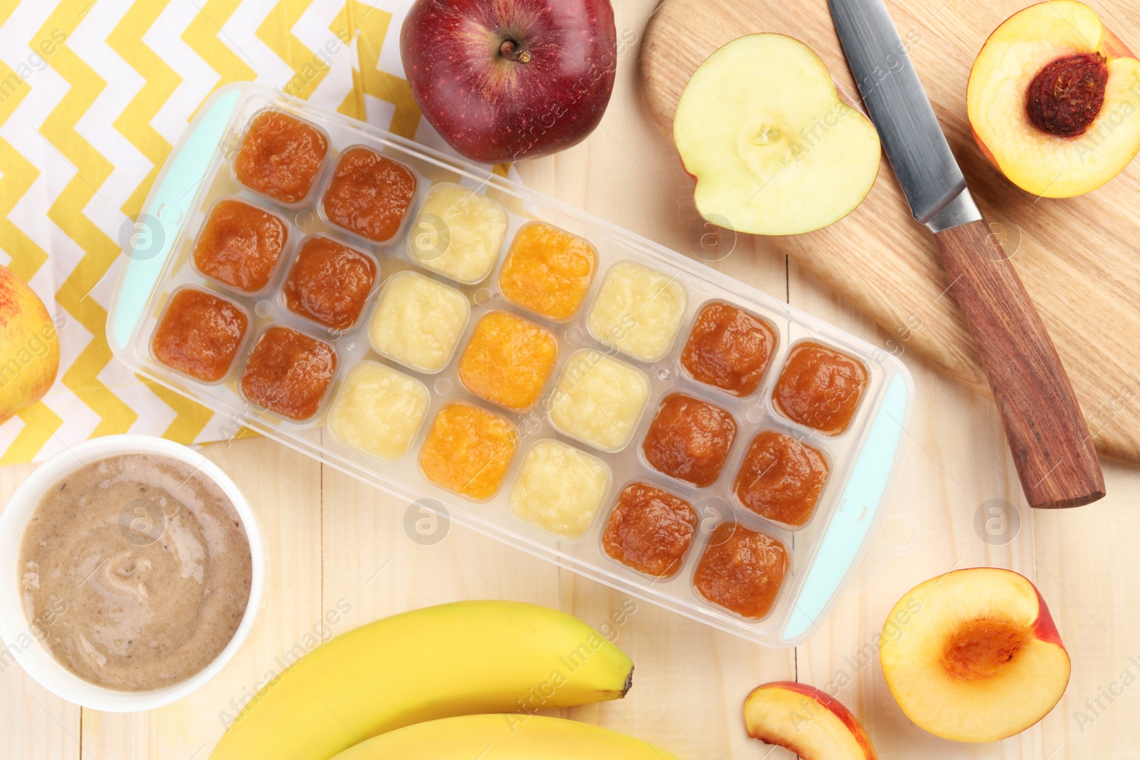 Photo of Different purees in ice cube tray and ingredients on wooden table, flat lay. Ready for freezing