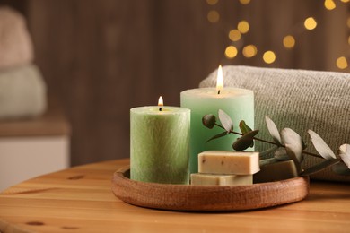 Photo of Spa composition. Burning candles, soap, towel and eucalyptus branch on wooden table, space for text
