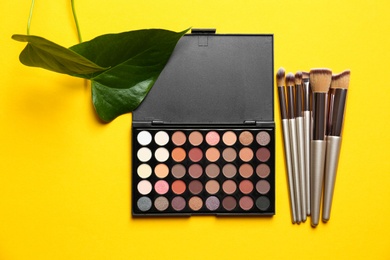 Photo of Flat lay composition with professional makeup brushes and eye shadow palette on yellow background