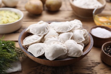 Photo of Raw dumplings (varenyky) and ingredients on wooden table, closeup