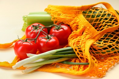 Photo of String bag with different vegetables on beige background, closeup