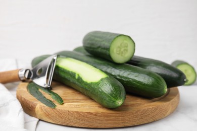 Fresh cucumbers and peeler on white table, closeup