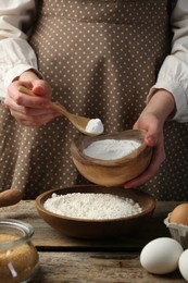 Making dough. Woman adding baking powder to flour at wooden table, closeup